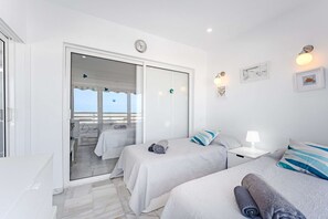 A hotel room with two beds, a balcony with a view, a clock, and wall-mounted lights. - Altamira 2bedr apartment with Sea view & A/C (Costa Adeje)