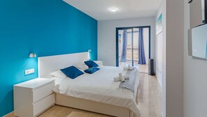 Un dormitorio con una cama blanca, almohadas azules y una mesita de noche blanca.