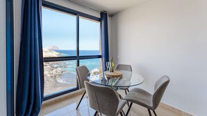 Un balcón con una mesa de vidrio y cuatro sillas, con vista a una costa rocosa.
