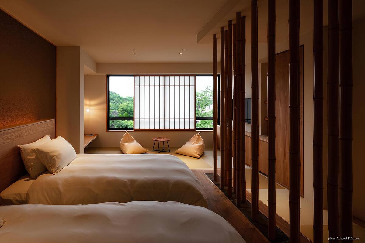 Quarto de hotel com duas camas, uma janela grande com vista para áreas verdes e um ecrã de bambu tradicional.
