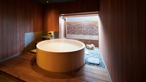 Un intérieur en bois avec une grande baignoire, une petite table et une fenêtre donnant sur une clôture en bois.