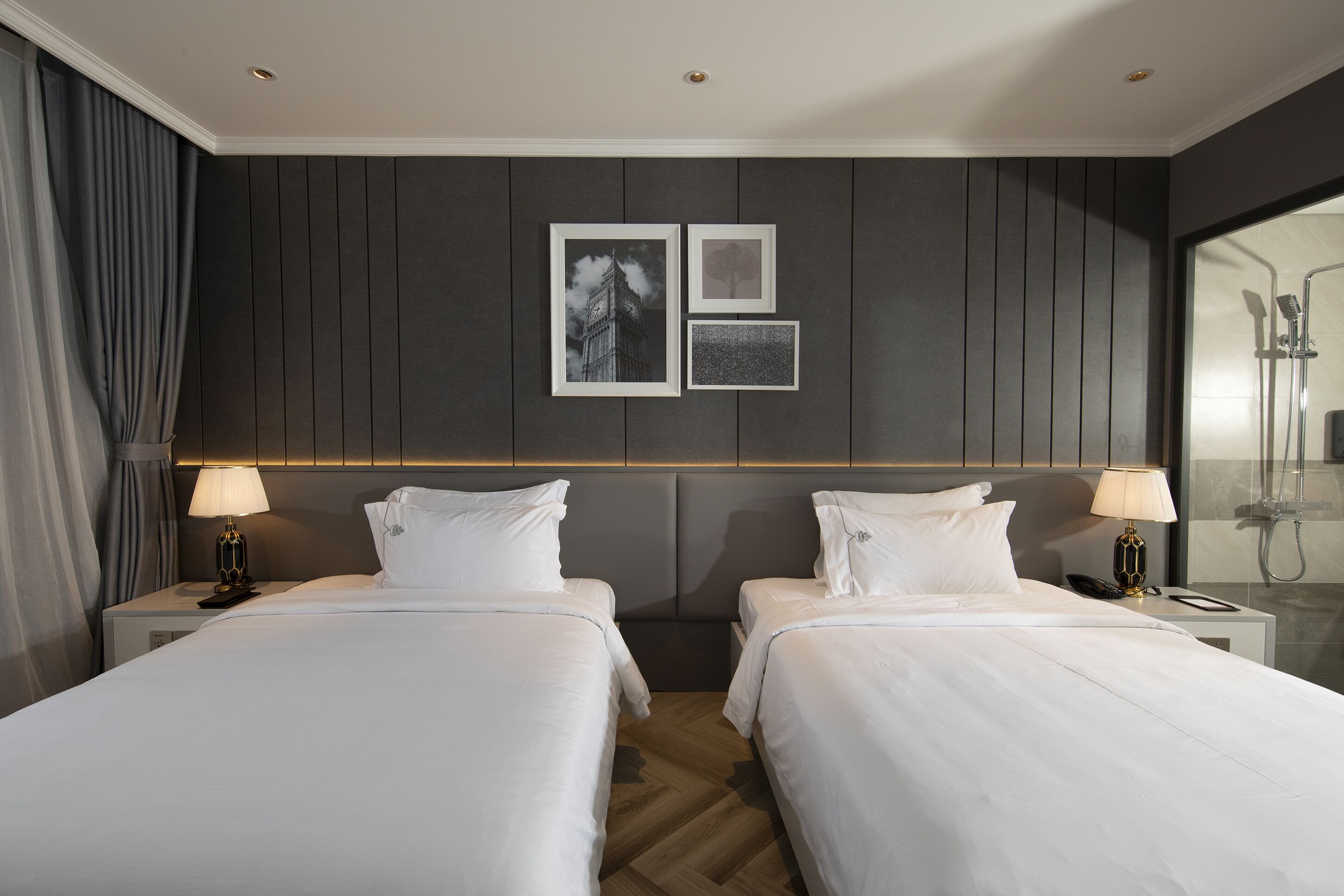 A hotel room with two beds, a shower area, and wall-mounted artwork.