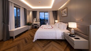 A hotel room with a large bed, bedside tables, a desk, and a view of the city.