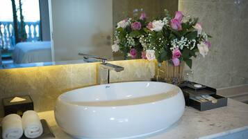 Un lavabo grande, blanco y ovalado con un grifo moderno, un espejo encima y un jarrón con flores rosas y blancas en la encimera.