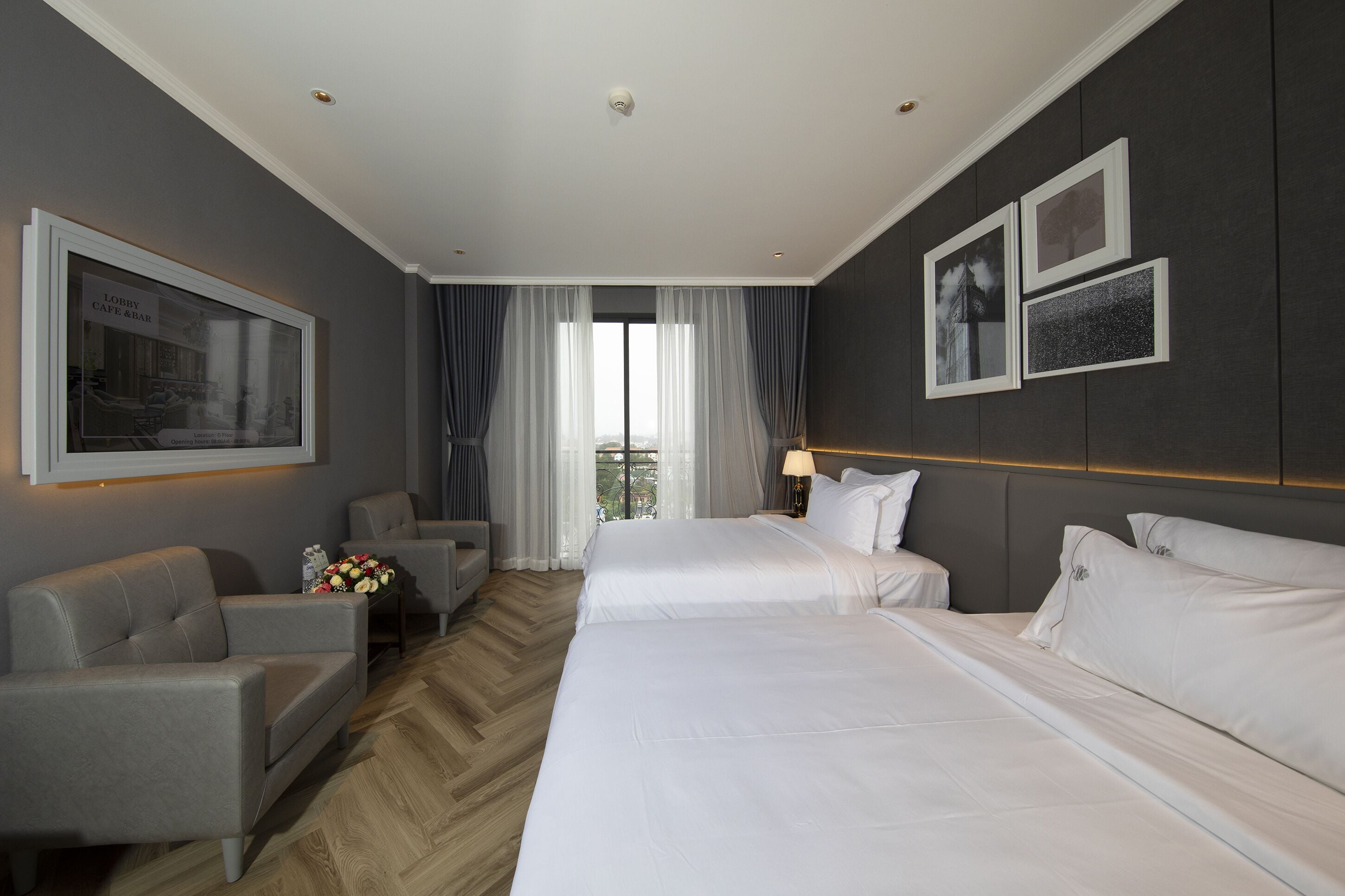 A hotel room with two beds, a sofa, a desk, and a view of the city through large windows.