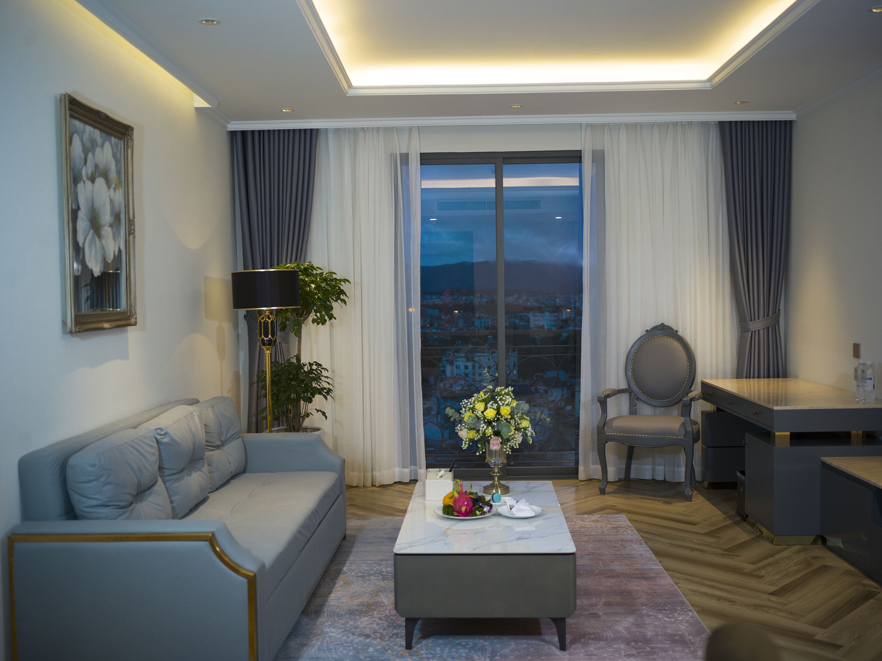 En moderne stue med sofa, sofabord med blomster, skrivebord og stol.