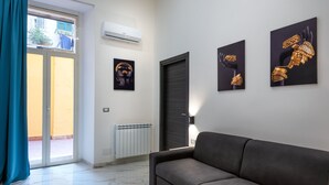 Un salon moderne avec un canapé, une porte-fenêtre coulissante donnant sur un espace extérieur et des œuvres d’art accrochées aux murs.