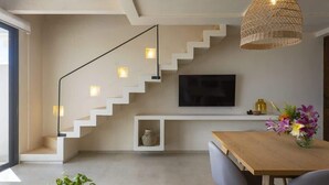 Uma sala de estar moderna com escada, televisão de tela plana na parede, mesa de jantar com cadeiras e luminária pendente.