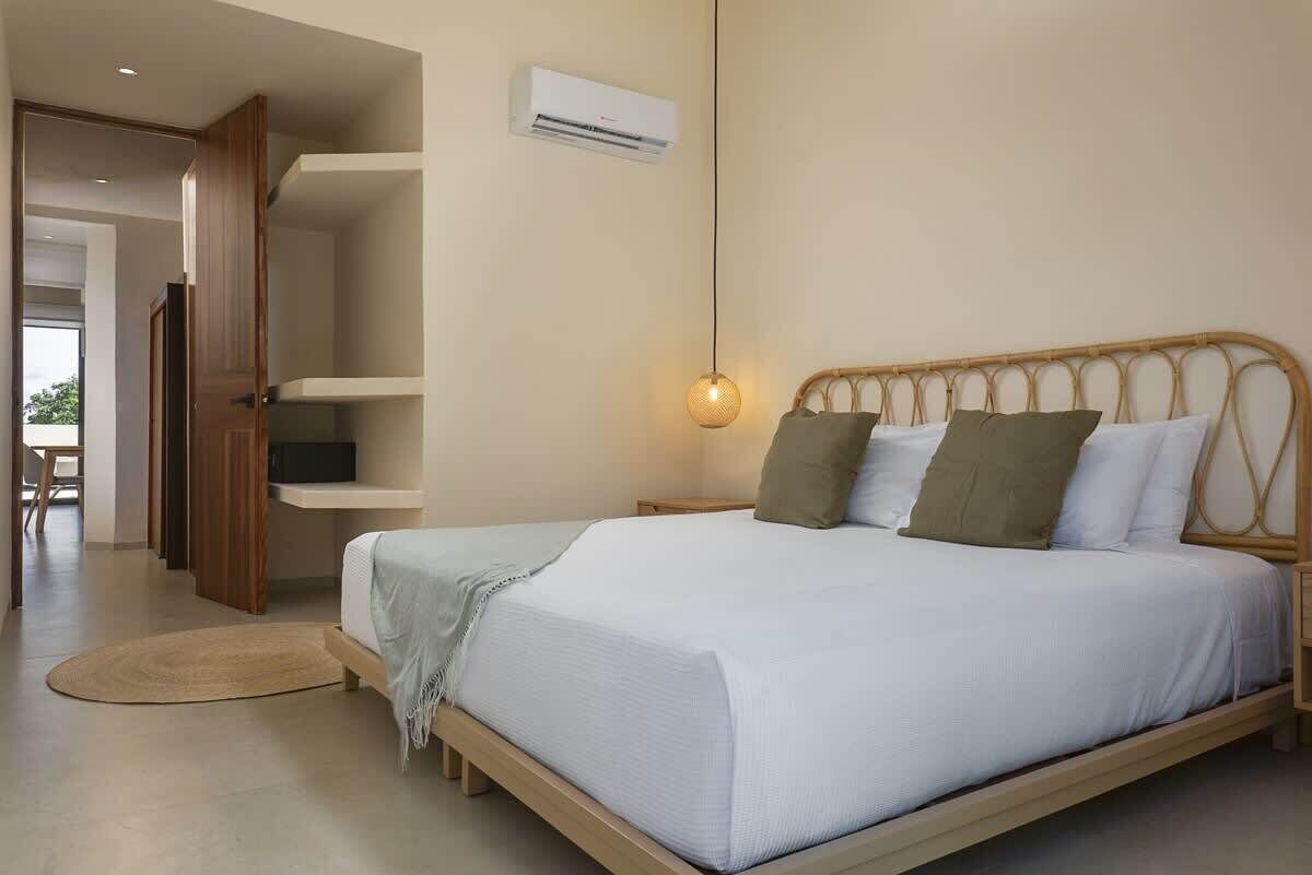 Une chambre à coucher comprenant un lit, des tables de chevet, un climatiseur fixé au mur et un luminaire suspendu.