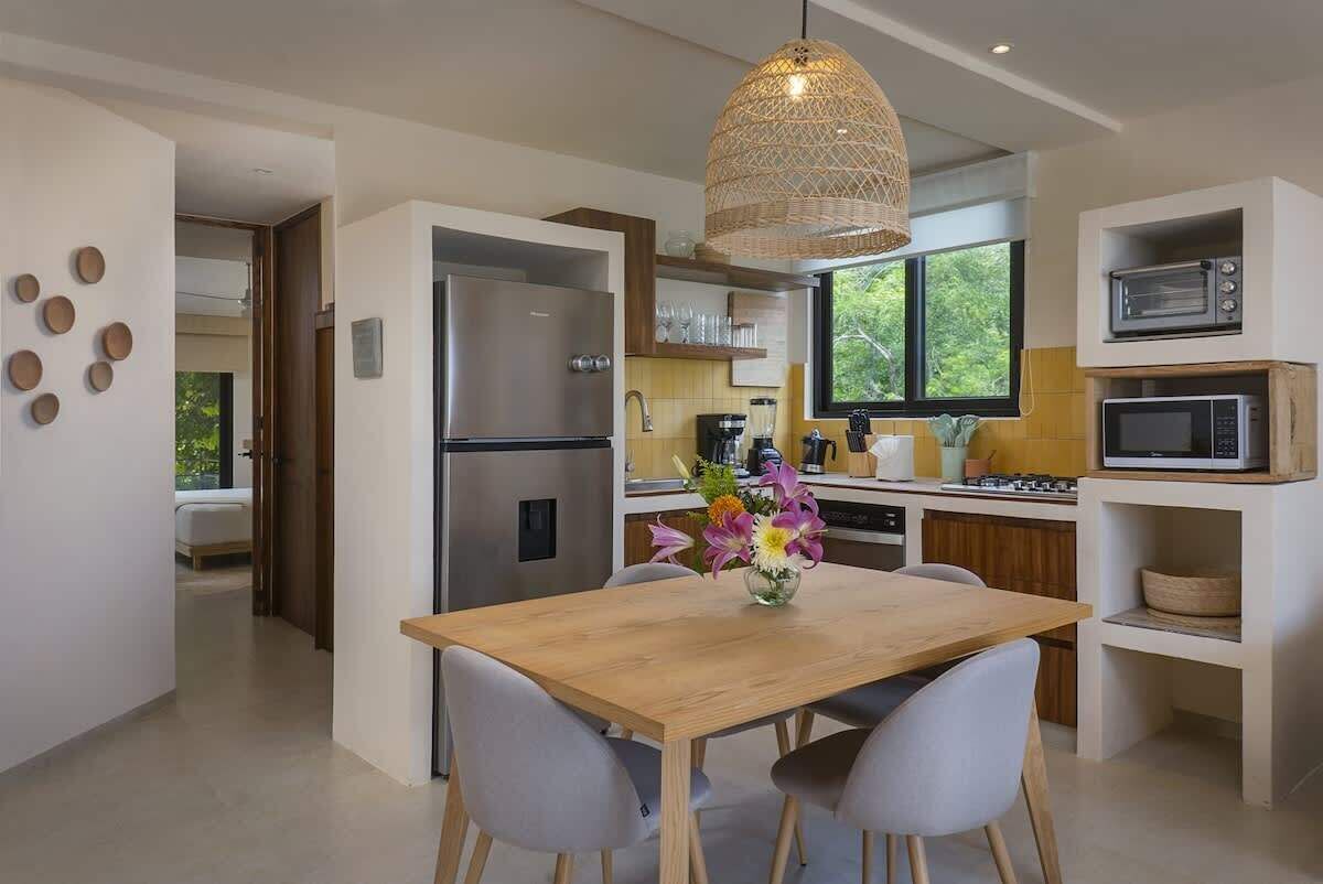 Una cucina moderna con un tavolo da pranzo in legno, sedie grigie, un frigorifero in acciaio inossidabile, forno integrato e una lampada a sospensione.