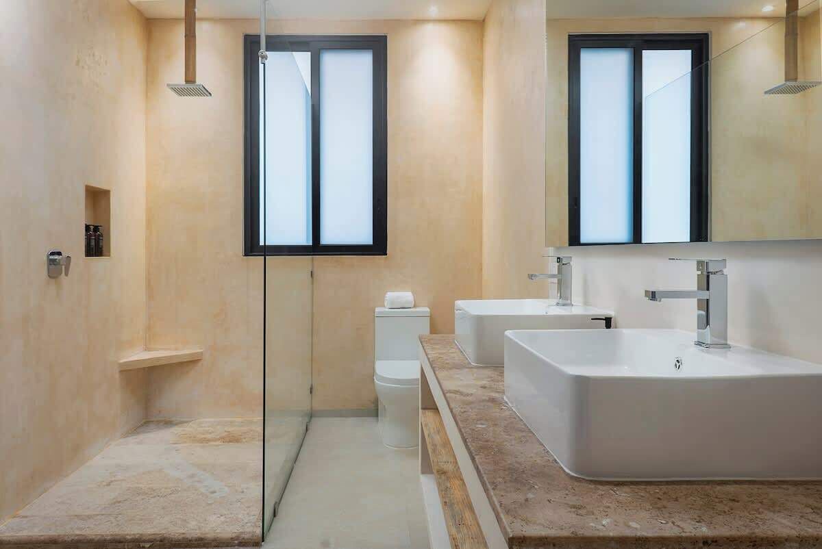 Un baño moderno con cabina de ducha de vidrio, dos lavamanos y un espejo grande.