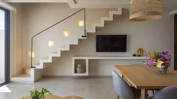 A modern living room with a staircase, a flat-screen TV, a dining table, and a potted plant.