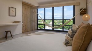 Een slaapkamer met een groot raam, een hangmat en uitzicht op groen.