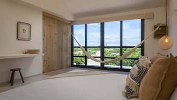 Ein Schlafzimmer mit einem großen Fenster, einer Hängematte und Blick ins Grüne.