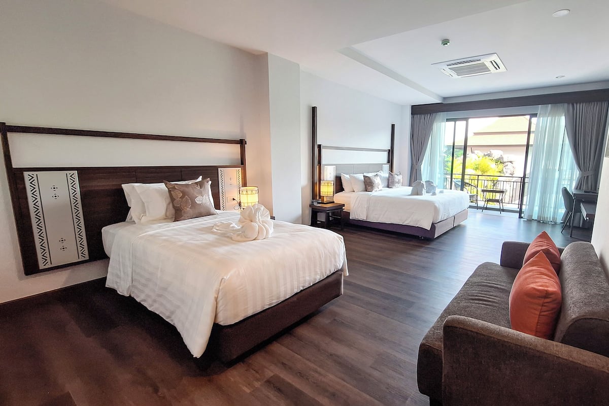 Une chambre d’hôtel avec deux lits, un canapé, un balcon avec vue et un ventilateur de plafond.