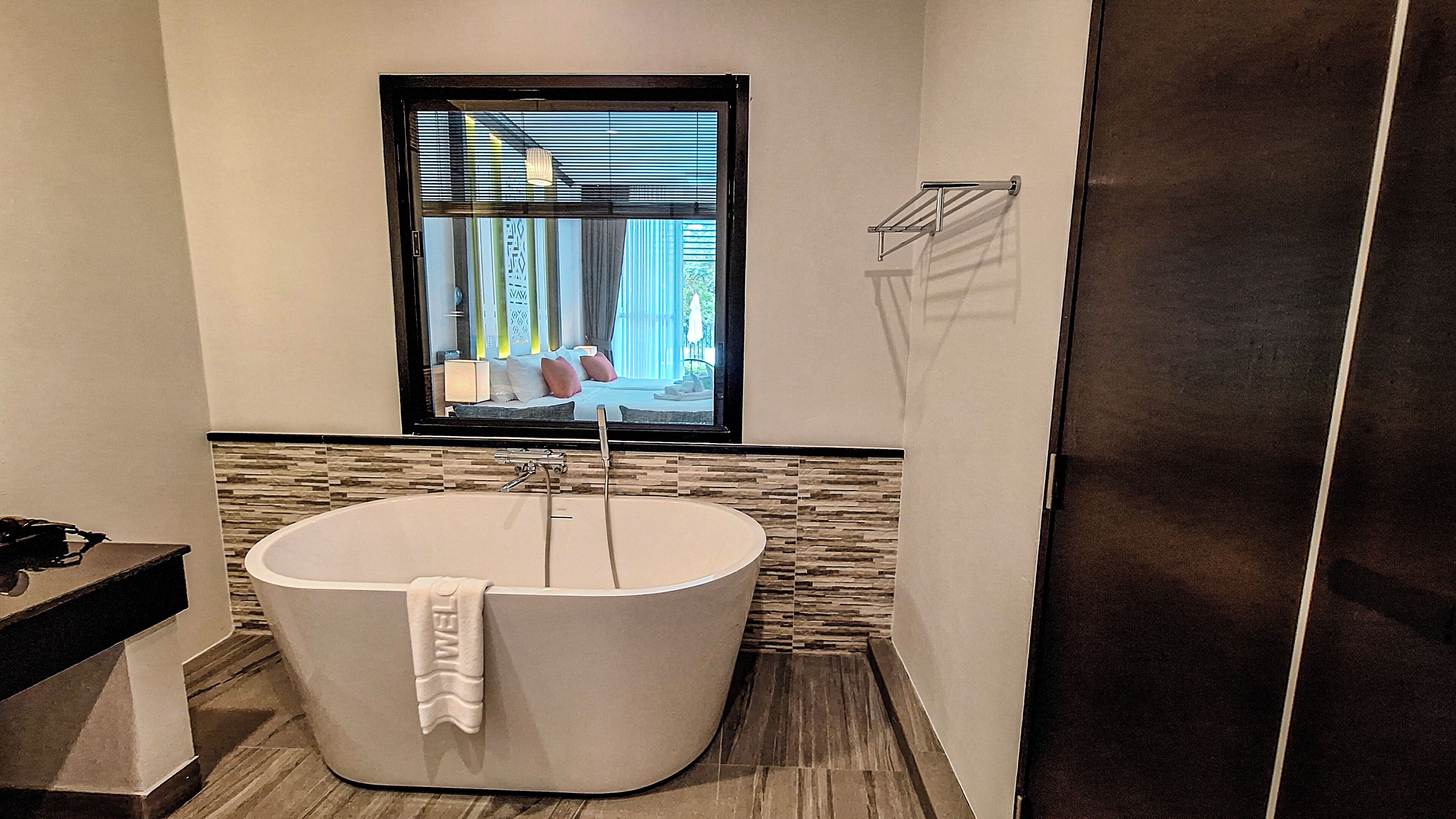 Un baño moderno con una bañera independiente, una ventana con persianas y un perchero para toallas.