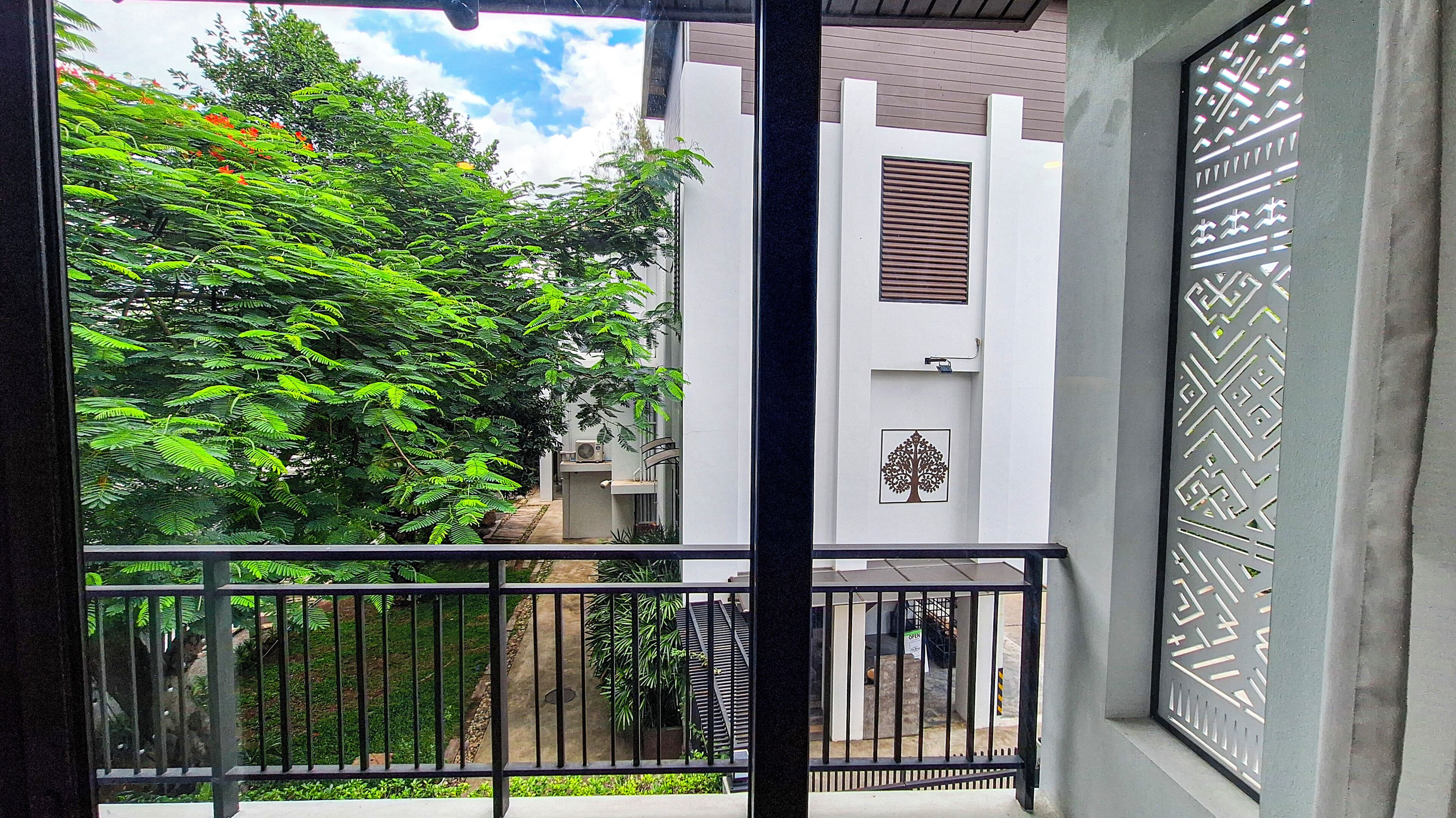 Uma varanda com vista para um edifício branco com o símbolo de uma árvore, guarda-corpo de metal e uma escadaria que leva a uma área externa.