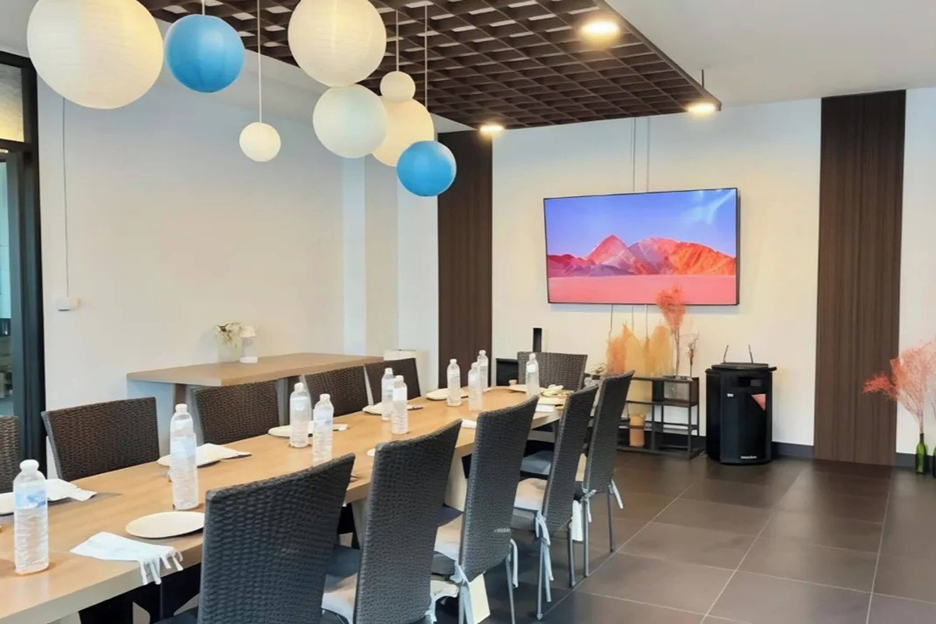 A conference room with a long table, chairs, water bottles, a TV screen, and decorative hanging lights.