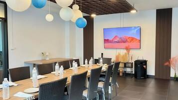A conference room with a long table, chairs, water bottles, a TV screen, and decorative hanging lights.