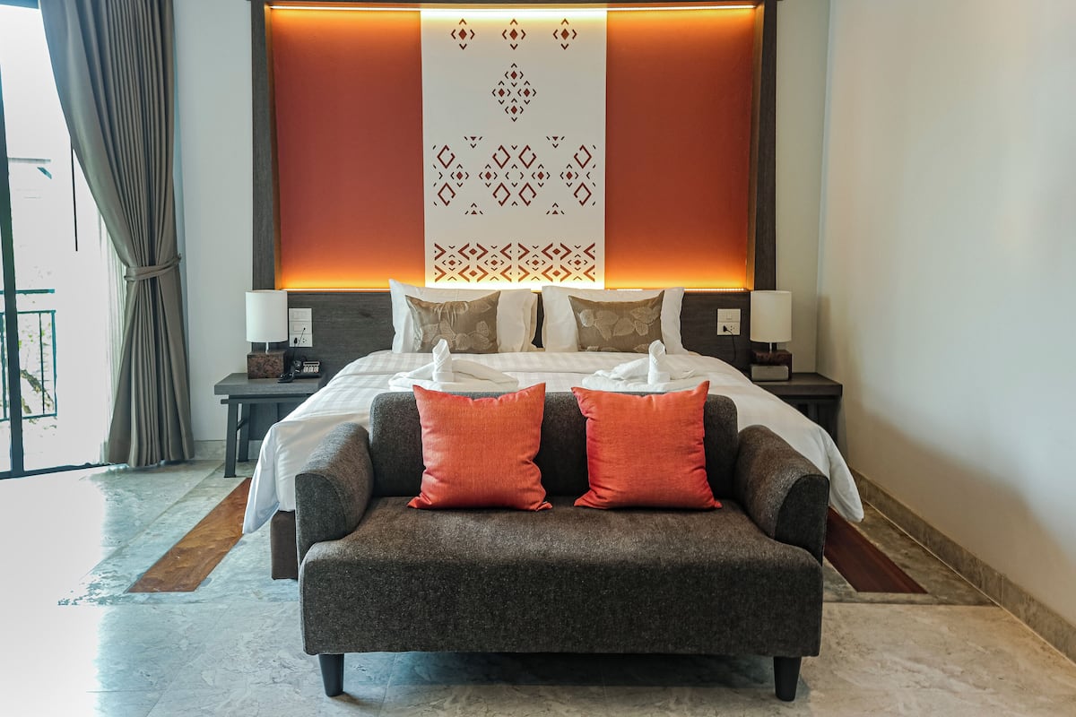 Une chambre d’hôtel avec un grand lit, deux tables de chevet, une petite table, un canapé et une vue sur l’extérieur.