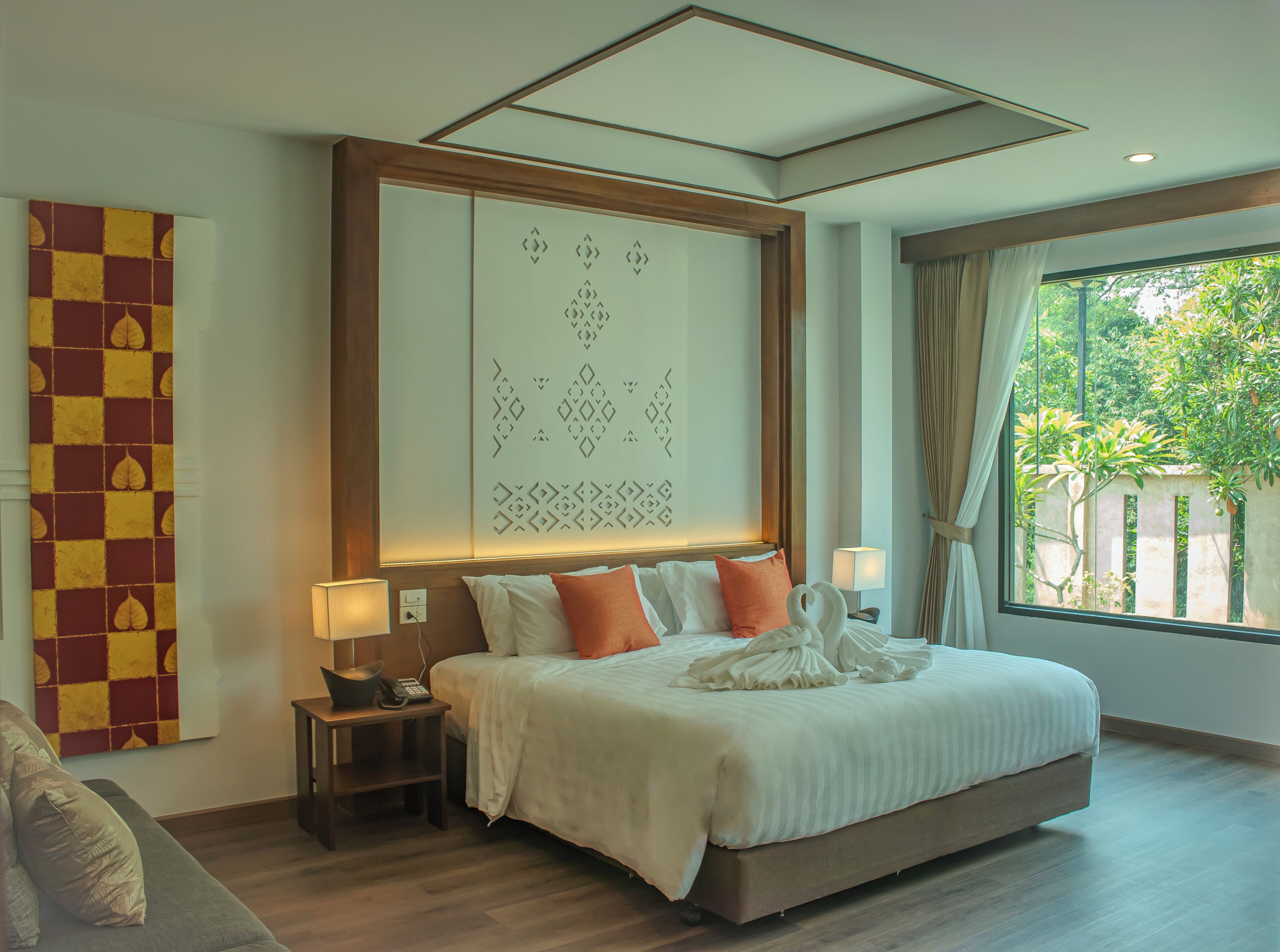 Une chambre d’hôtel avec un grand lit, deux tables de chevet, un panneau décoratif au mur et une fenêtre donnant sur un paysage verdoyant.