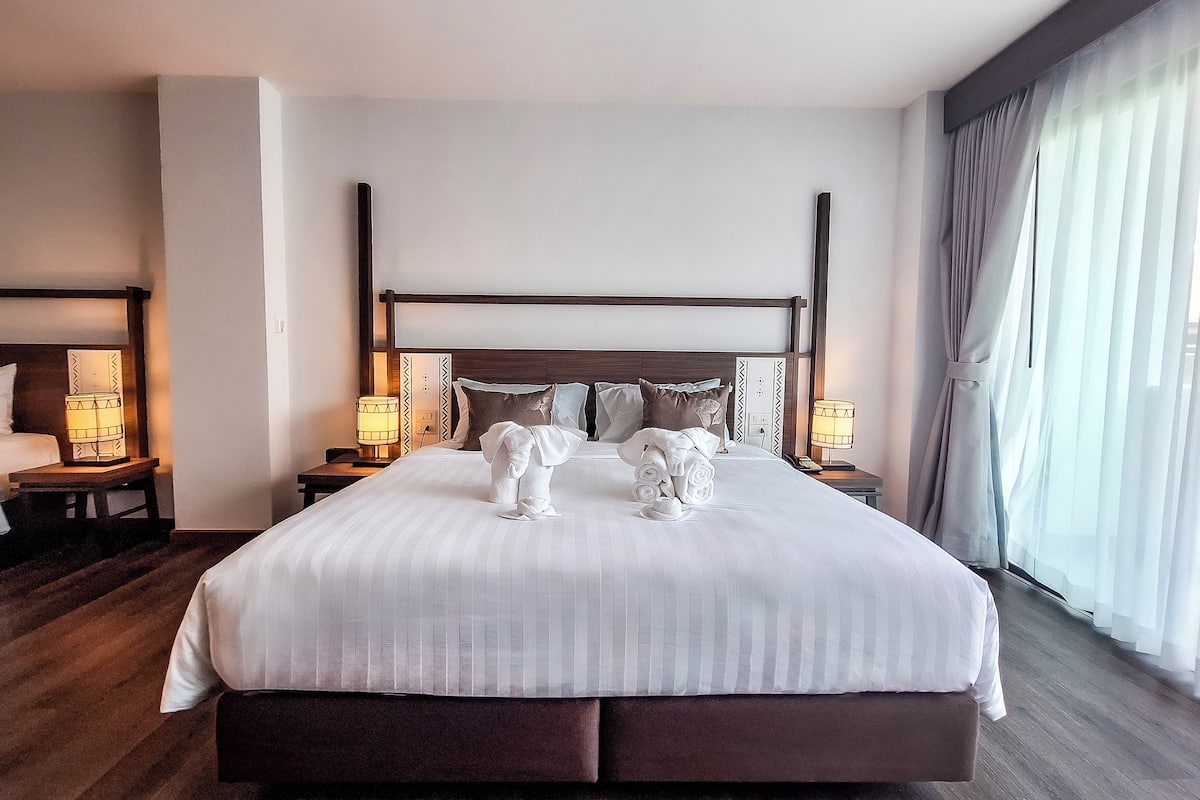 Un grand lit avec une tête de lit en bois, deux tables de chevet avec des lampes et une grande fenêtre avec des rideaux.