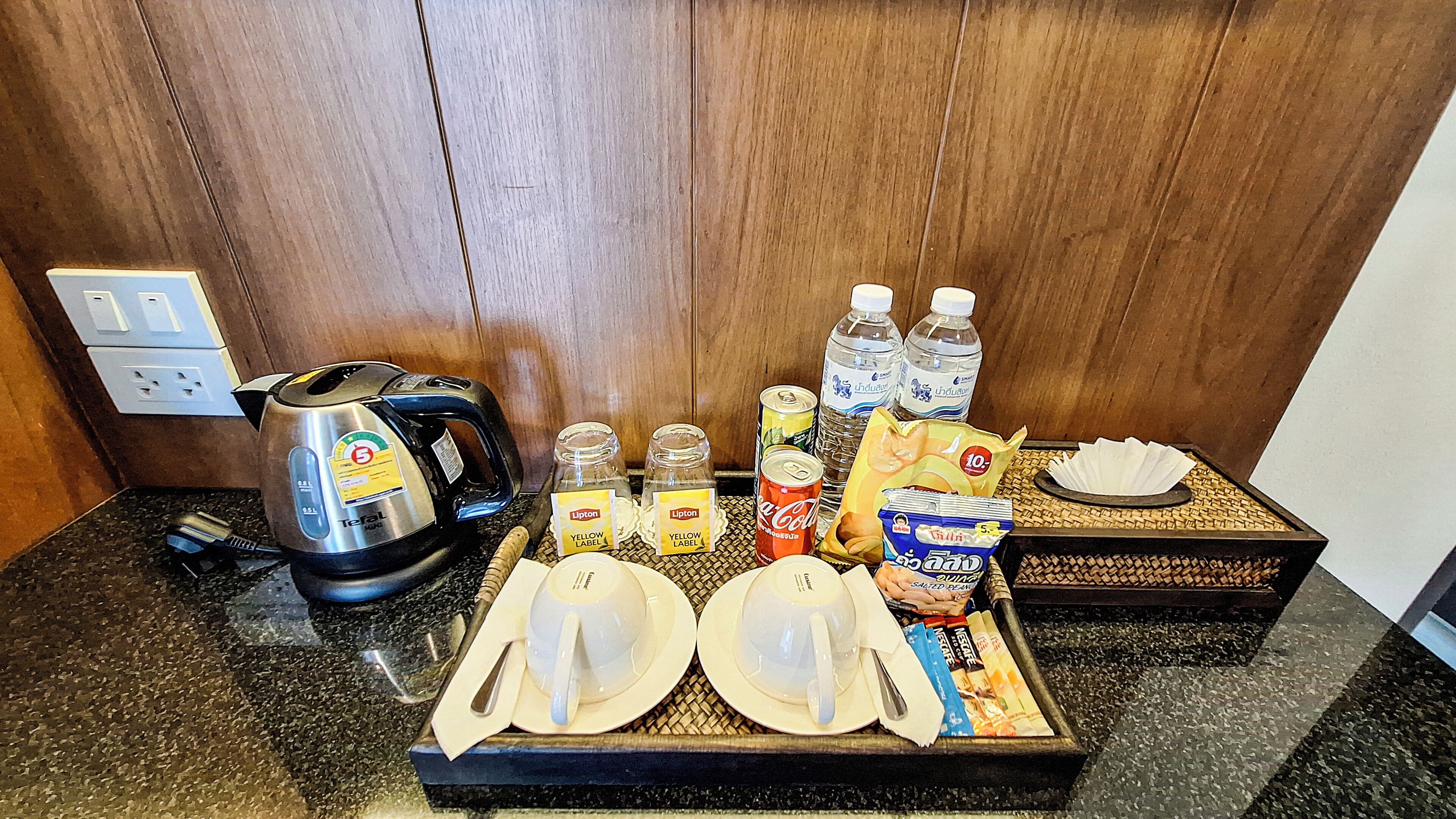 A kitchenette with a kettle, water bottles, Lipton tea, a can of soda, and a tray with plates and utensils.