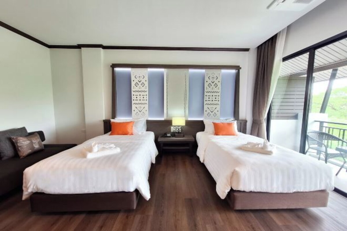 Quarto de hotel com duas camas, um sofá, uma mesa de cabeceira e uma varanda.