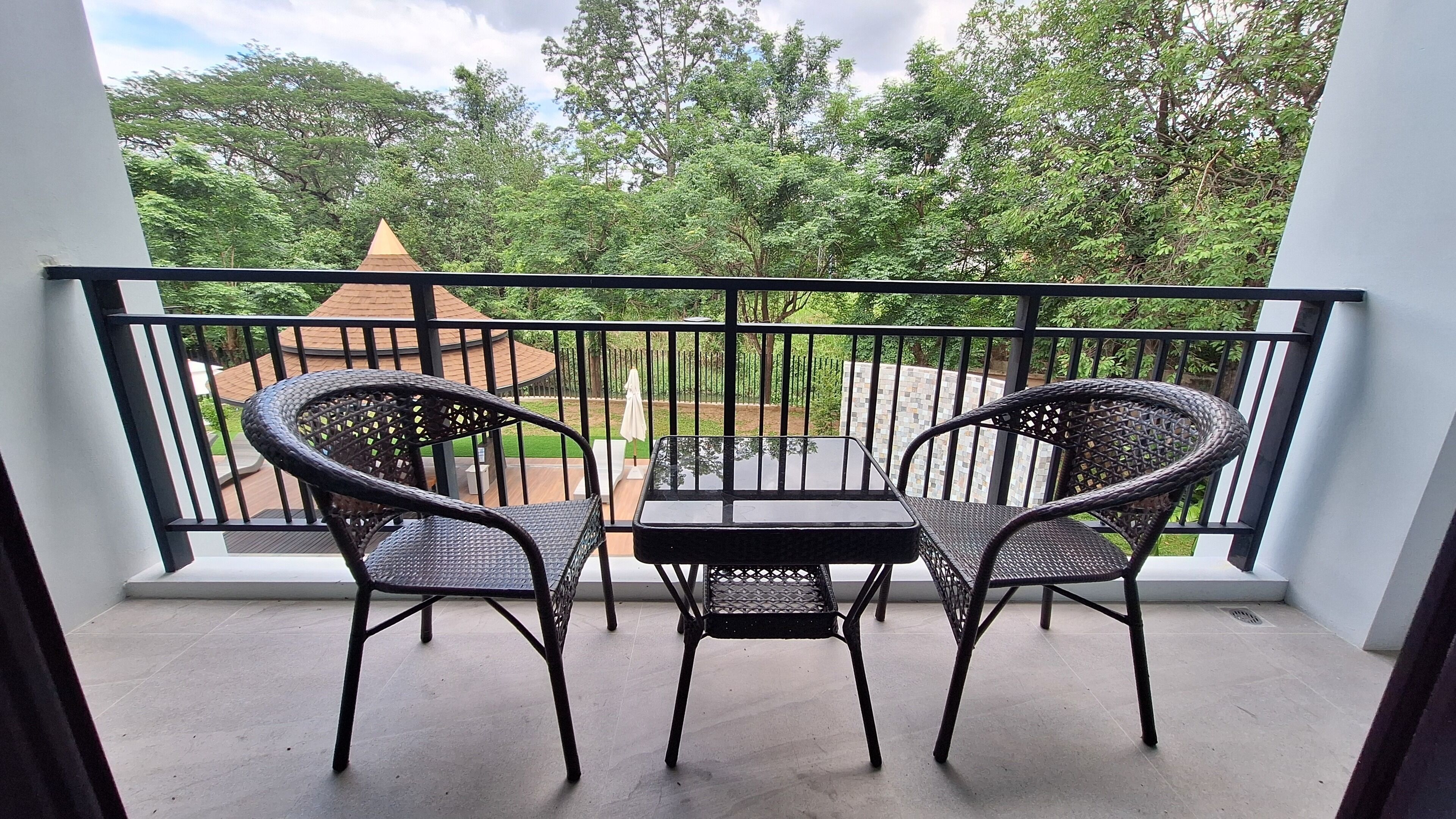Un balcon avec deux fauteuils en osier et une petite table, donnant sur un jardin agrémenté d’un kiosque.