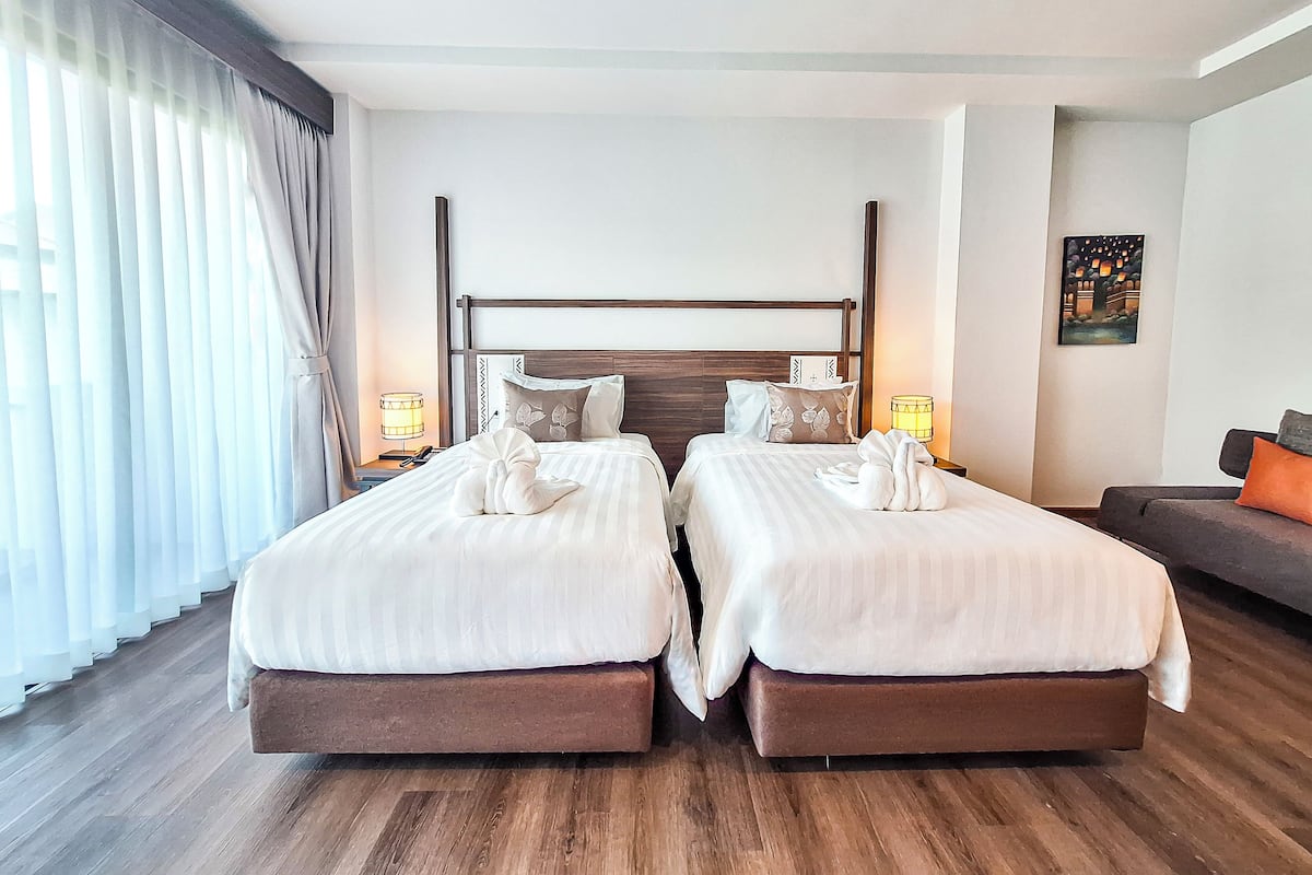 Une chambre d’hôtel avec deux lits, un plancher en bois, une table de chevet avec une lampe et un tableau au mur.
