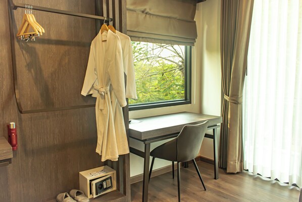 Une pièce avec un plancher en bois, un bureau avec une chaise, une fenêtre avec des rideaux et un peignoir suspendu à un porte-manteau.
