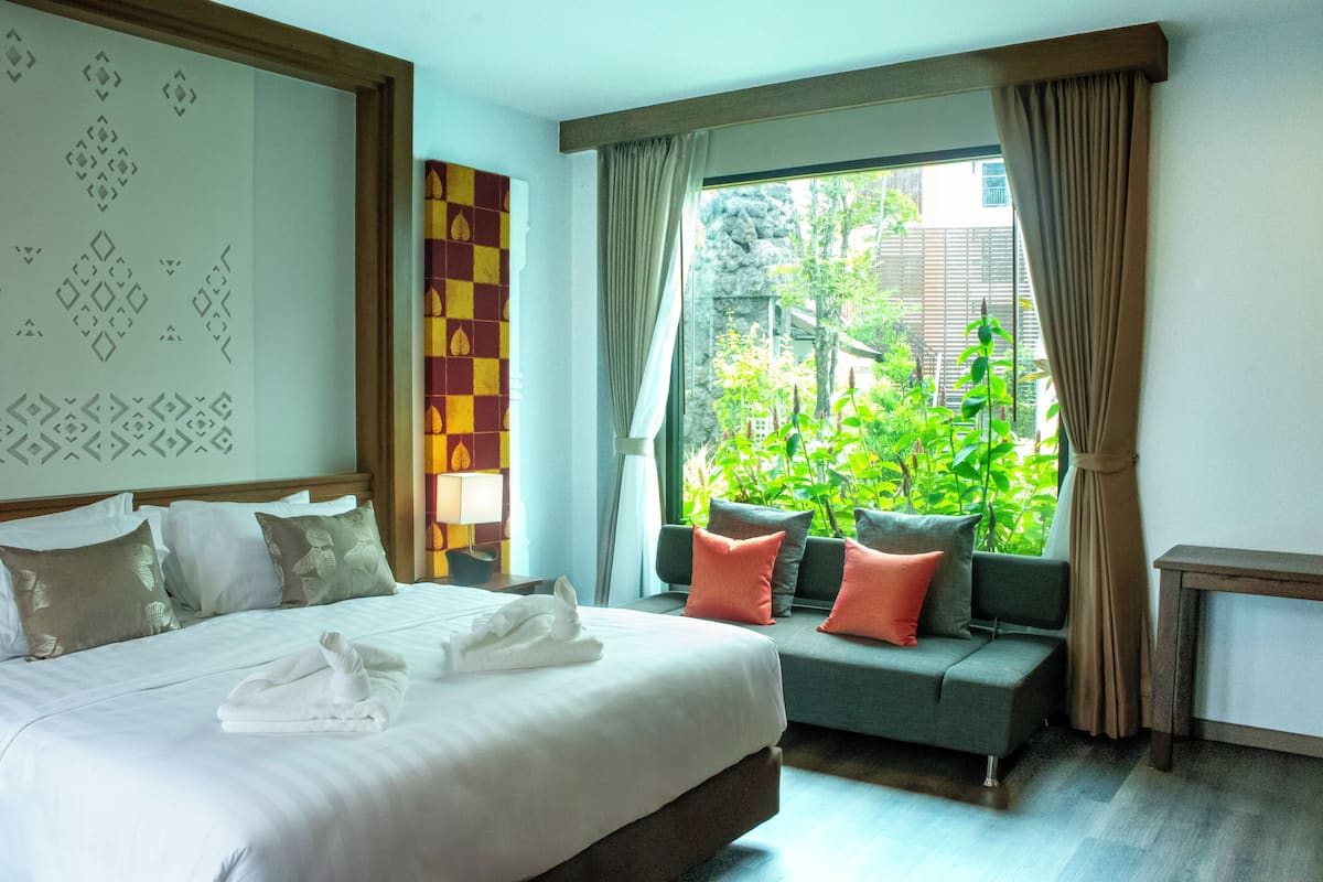 Une chambre d’hôtel avec un grand lit, un canapé, une fenêtre avec des rideaux et une vue sur la verdure.