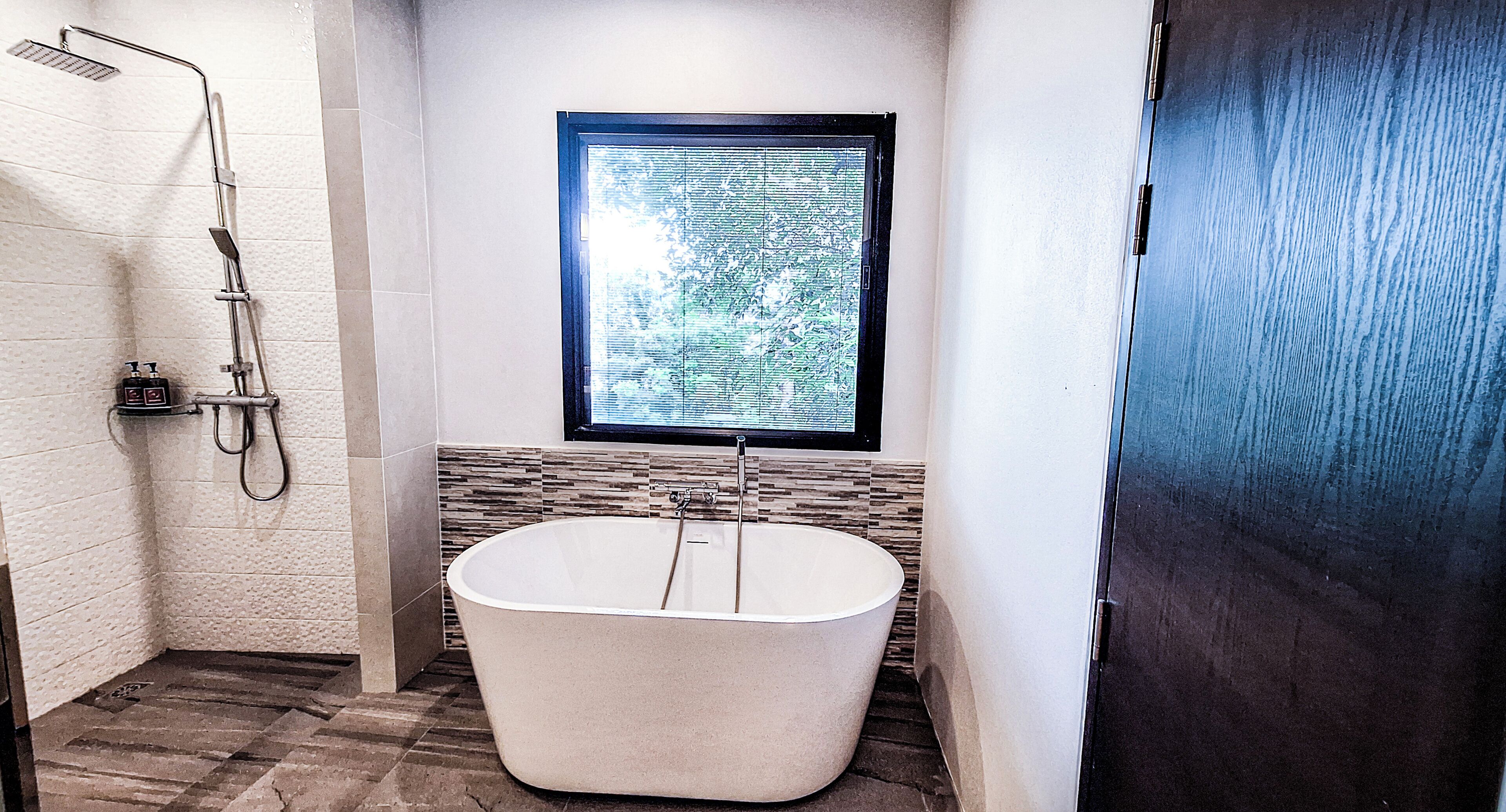 A modern bathroom with a freestanding bathtub, a shower area, and a window providing natural light.