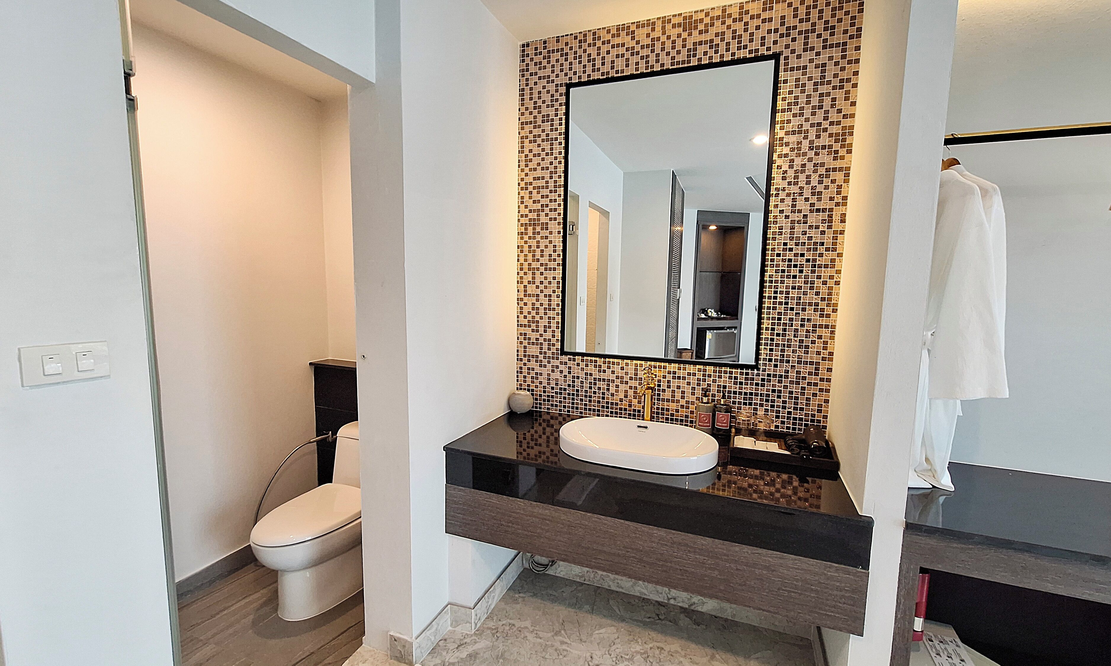Ein modernes Badezimmer mit schwarzem Waschtisch, weißem Waschbecken und einer Wand mit Mosaikfliesen.