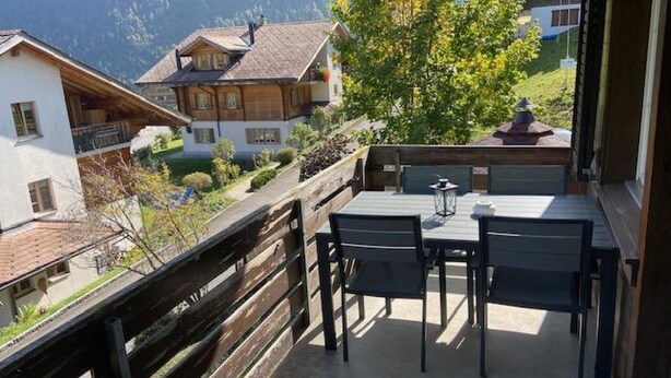 Un balcon avec une table et des chaises, d’où l’on peut admirer une montagne et un village.