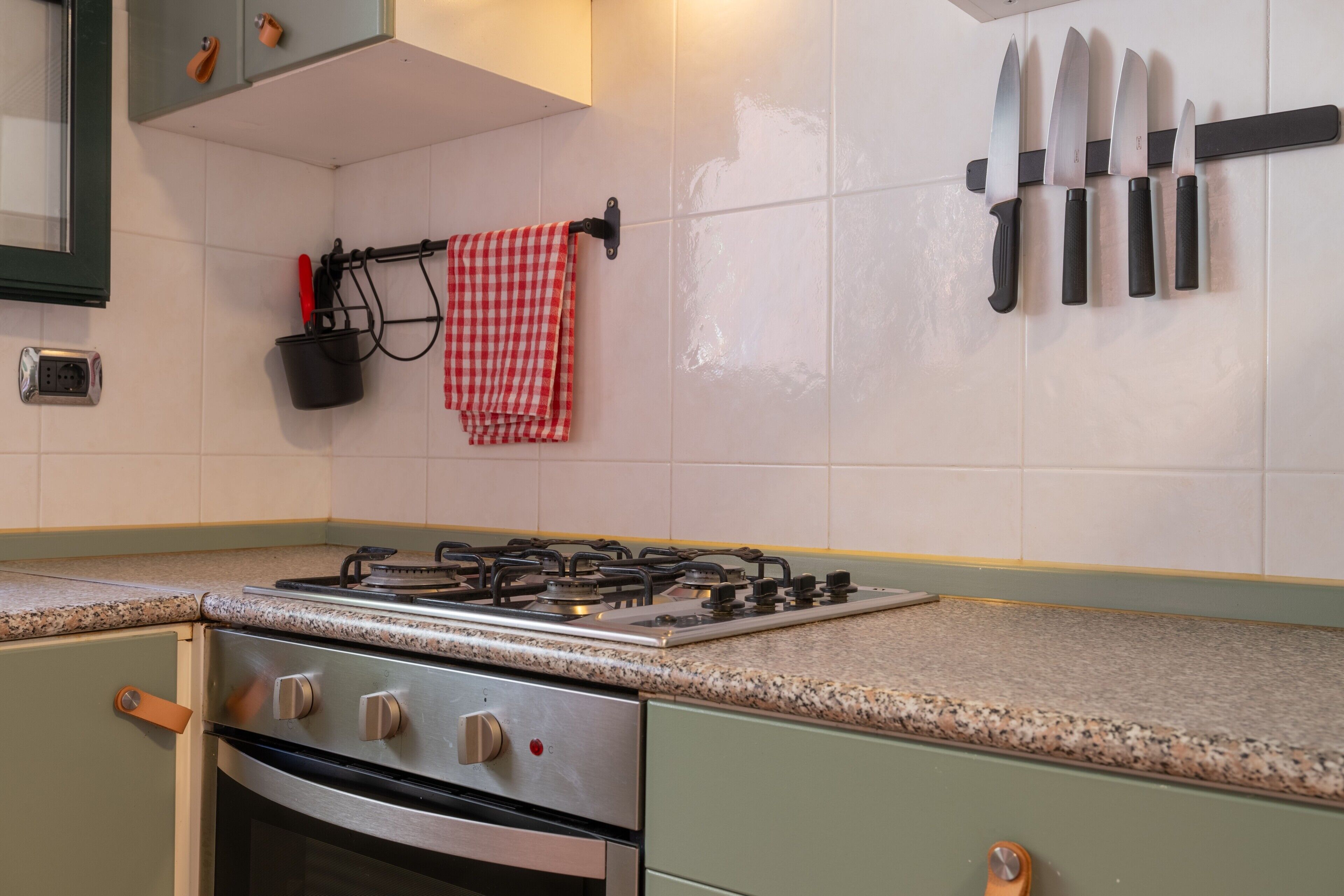 Uma cozinha com fogão a gás, forno e um porta-facas na parede.