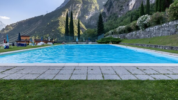 Ein Schwimmbad mit Blick auf eine Bergkulisse, umgeben von einer Steinmauer und Grünpflanzen.