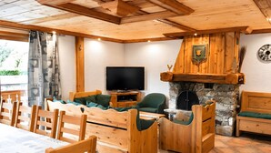 A wooden interior with a stone fireplace, a television, and a dining area with wooden furniture. - Apartment "Les Dolomites" with Mountain View, Private Terrace and Wi-Fi (La Plagne-Tarentaise)