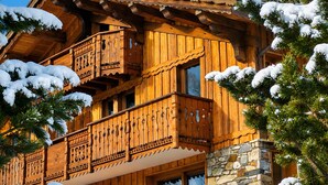 A wooden chalet with a balcony, stone foundation, and snow-covered surroundings. - Apartment "Les Dolomites" with Mountain View, Private Terrace and Wi-Fi (La Plagne-Tarentaise)