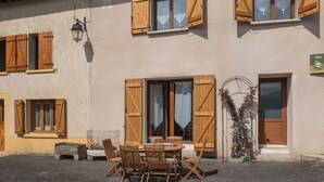 Un edificio con contraventanas de madera, una mesa con sillas y una puerta con un letrero.