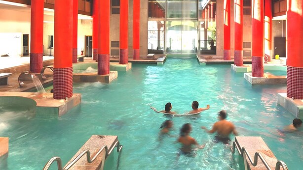 Una piscina interior con varias pistas, pilares rojos y una zona de visualización central.