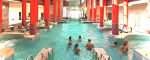 Une piscine intérieure dotée de plusieurs couloirs, de piliers rouges et d’un espace central aménagé pour les spectateurs.