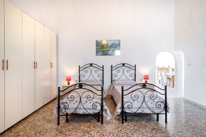 Une chambre avec deux lits, une armoire, un tableau et une vue sur une autre pièce.