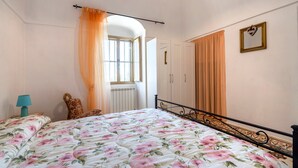 A bedroom with a bed, a chair, a wardrobe, and a window with curtains.