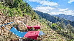 Dos sillones de descanso con toallas rojas, un muro de piedra y vista a un paisaje montañoso.