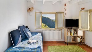 Un dormitorio con cama, televisor, estantería y ventana con vistas a la montaña.