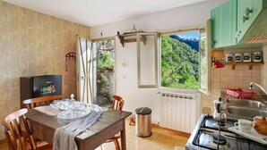 Una cocina con vista a un bosque, una mesa de comedor con sillas, una estufa y un cubo de basura.
