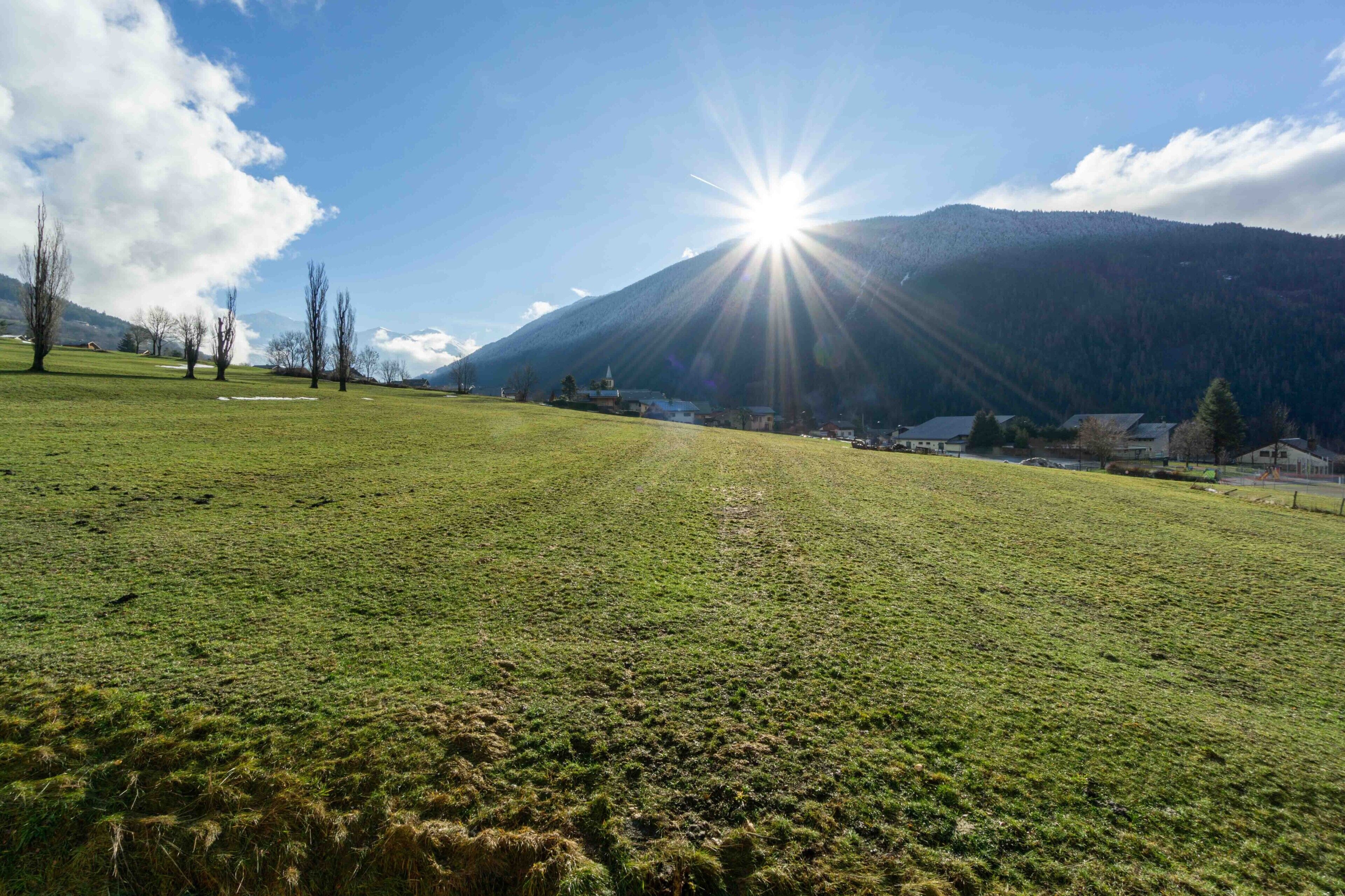 Un campo cubierto de césped con una montaña al fondo y un sol brillante.
