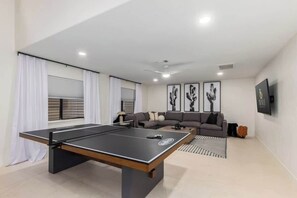 Une table de ping-pong dans un salon moderne, avec un canapé et des œuvres d’art accrochées aux murs.