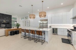 A modern kitchen with white cabinets, a stainless steel refrigerator, and a bar area with stools. - Anderson LUX Estate/Private Bar&Pool/Sleeps 12 (Scottsdale)